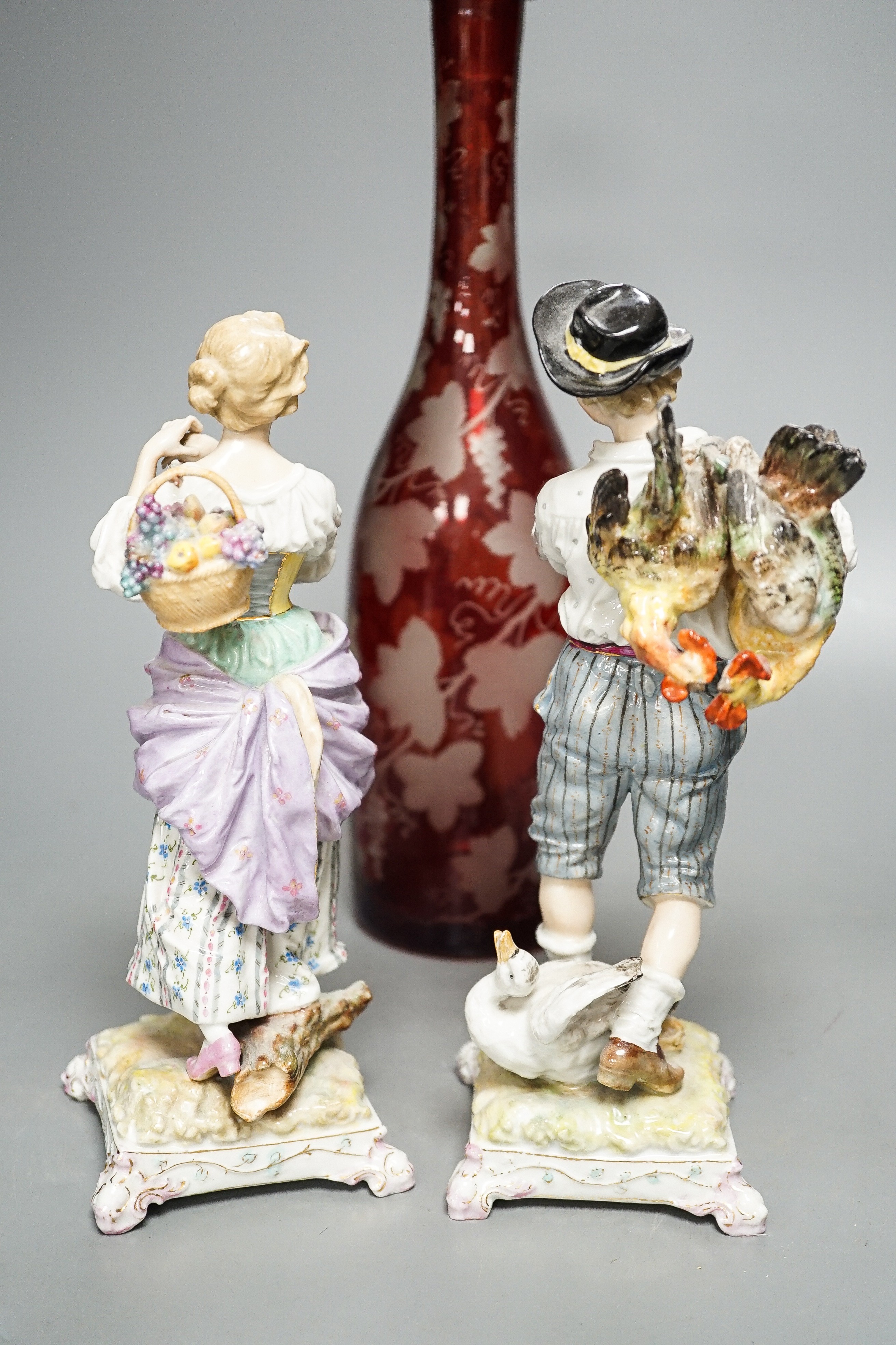 A late 19th century Bohemian wheel engraved ruby glass decanter and a pair of continental porcelain figures, decanter 37 cms high, including stopper.